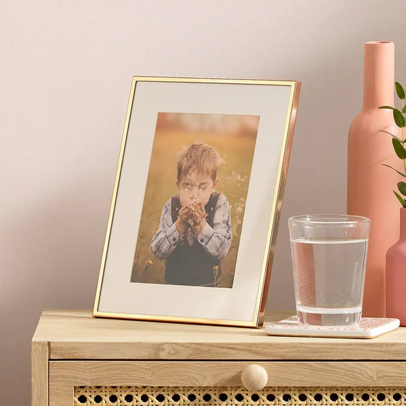 Framed photo of a child on a wooden side table with a glass of water and pink vase.