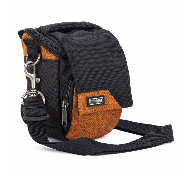 A black and orange crossbody camera bag with a textured orange front pocket, black flap, and silver metal clasp, shown on a white background.